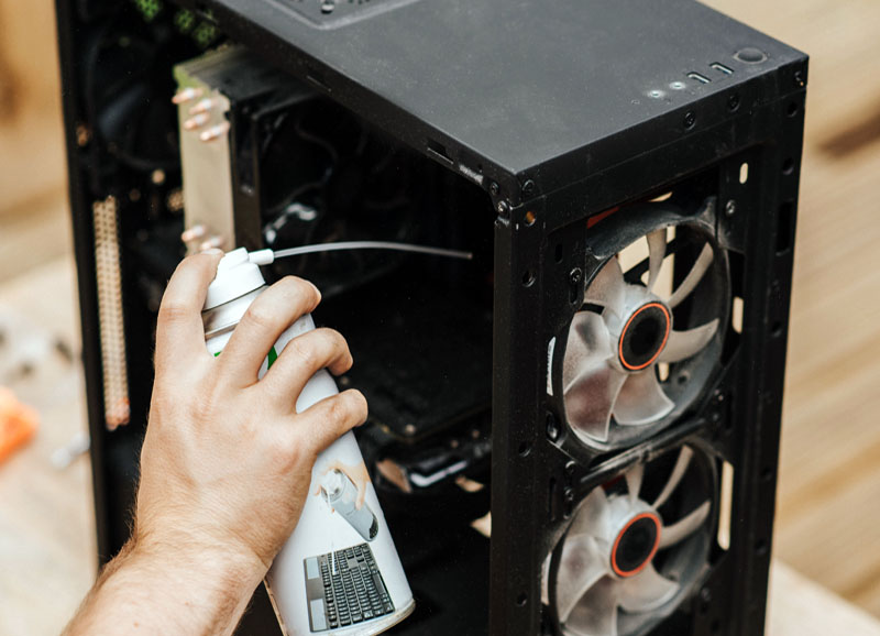 A man's hand squirts compressed air into a disassembled computer hub. MNK